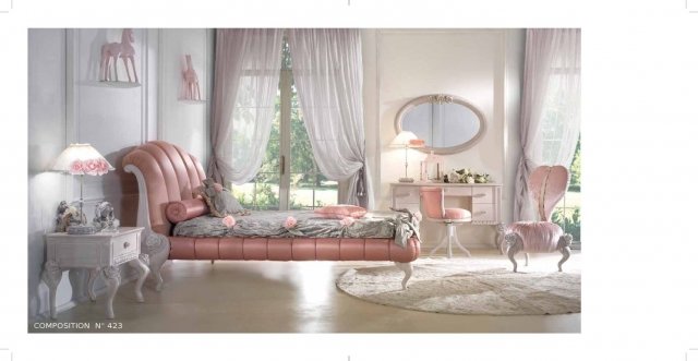 This picture is of an opulent and luxurious bedroom with a large King size bed in the center of the room. The walls are a light beige color, while the trim, doors, and flooring are a darker wood color. The bed is upholstered in an ivory tufted fabric with white linens and pillows. On both sides of the bed are two crystal nightstands, and across from the bed is an ornately carved armoire. There is a plush white rug underneath the bed, and two matching chairs on either side of the bed. The lighting