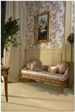 This is an interior rendering of a luxurious bed and breakfast style bedroom. The room features a lavish four-poster bed with detailed carvings, a comfortable armchair, a set of upholstered sofas and a desk. The walls are painted in a soothing shade of beige with floor-to-ceiling curtains framing the windows. Adorning the walls are art pieces and a gorgeous chandelier overhead. The floor is finished in a deep hardwood that adds a rustic charm to the otherwise glamorous space.