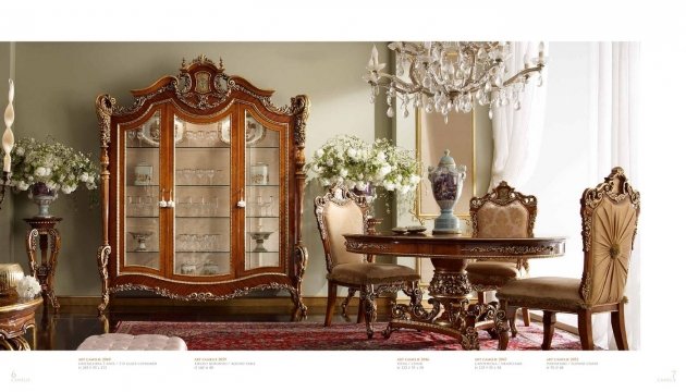 This picture shows an interior design of a luxurious living room. The room is decorated with classic and modern furniture, including a white couch, an armchair, and a wooden table. The walls are painted a light beige color and feature a bold, black and white striped wallpaper. The walls are also decorated with several artworks and mirrors. The overall effect is one of grandeur and elegance.