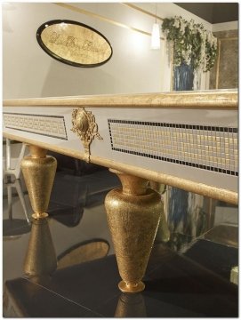 This picture shows a luxurious bathroom featuring a white marble vanity with double sinks, a wall-mounted mirror, and gold fixtures. The room is decorated with a velvet settee and gold sconces, and the floor is covered with a beige patterned rug.