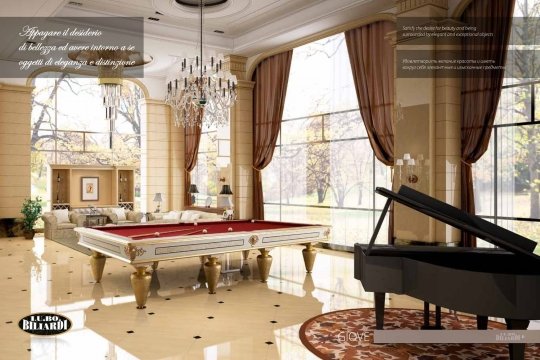 The picture shows an ornately decorated living room designed in a luxury style. The room features a large U-shaped cream colored sofa with four accent pillows, a glass-topped coffee table, and a marble-topped side table. On top of the side table is a crystal vase filled with fresh flowers. Completing the room are a luxurious chandelier, white and gold curtains, and a beautiful area rug.