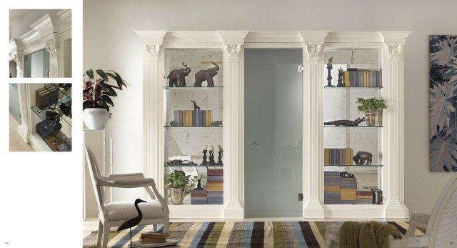 This picture shows a beautiful modern living room space with a luxurious light grey marble fireplace surrounded by shelves and artwork. The room also has a white couch, a black leather armchair, a velvet ottoman, and a glass coffee table. The walls are a light, neutral color, and the floor is a light wood. There are several hanging lamps in the room, which adds to the elegant atmosphere.