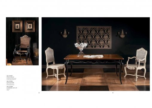 This picture shows a luxurious modern dining room. The walls are light grey and white with decorative moulding at the top, and a panel of wallpaper with a pink, purple and orange pattern. The dining table is round and rests on a white and gold base. The chairs have curved white frames with velvet upholstery in light grey and rose. There is a gold-crowned chandelier hanging from the ceiling, and the room is framed by large windows.